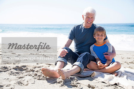 Portrait of grandfather and grandson, sitting on beach, smiling