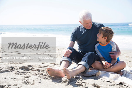 Grandfather and grandson sitting on beach, smiling