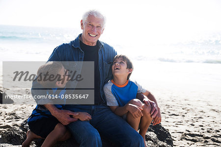 Grandfather with two grandsons, sitting on beach, smiling