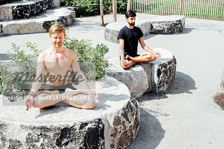 Two men meditating in lotus pose on park stone seats