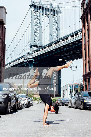 Man practising yoga handstand in front of Manhattan Bridge, New York, USA
