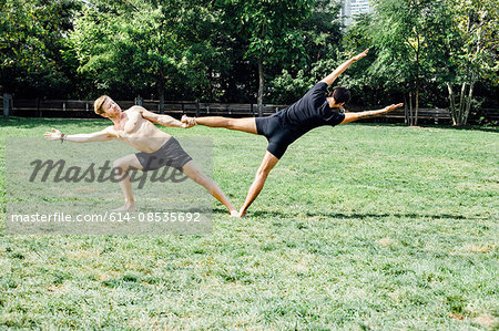 Two men practising yoga foot hold position in park