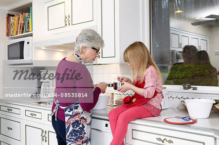 Girl and grandmother looking into saucepan at kitchen counter