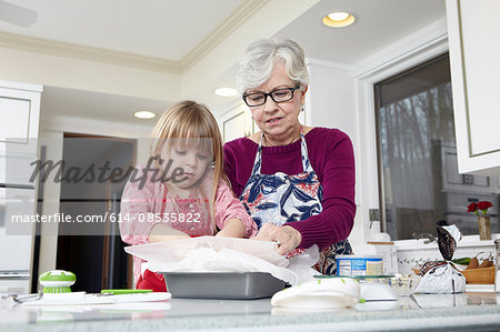 Girl and grandmother preparing greaseproof paper at kitchen counter