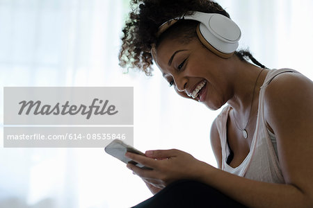 Woman wearing headphones, looking at smartphone, laughing