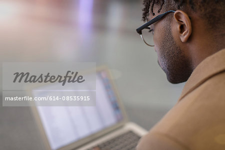 Over shoulder view of young businessman sitting in train station using laptop