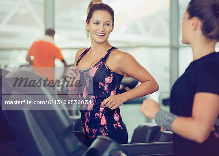 Smiling women talking on treadmills at gym
