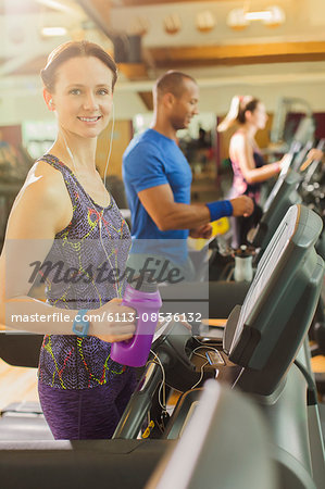 Portrait smiling woman with water bottle on treadmill at gym