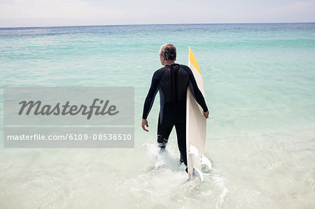 Senior man walking towards sea with a surfboard