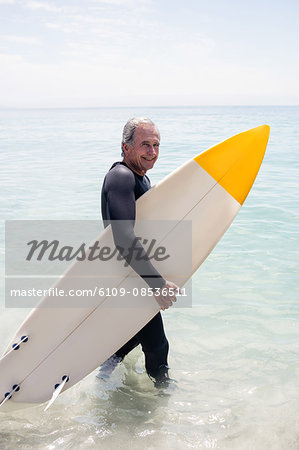 Happy senior man in wetsuit holding a surfboard