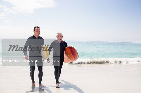 Happy father and son in wetsuit walking with surfboard