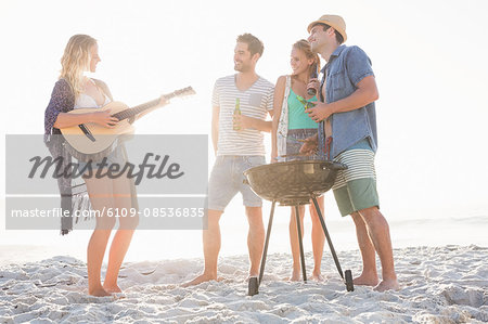 Cute group of friends having a barbecue and beers and playing the guitar