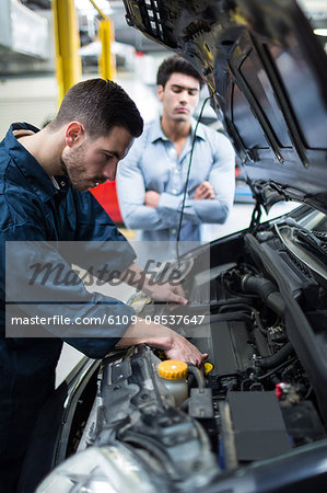 Mechanic examining car engine while customer standing and looking