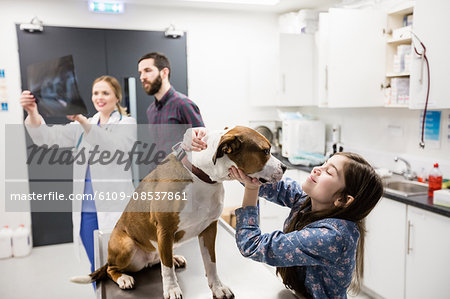 Girl playing with her pet dog while vet discussing x-ray in background