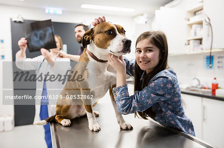 Girl playing with her pet dog while vet discussing x-ray in background