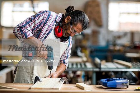 Carpenter drilling a hole in a wooden plank