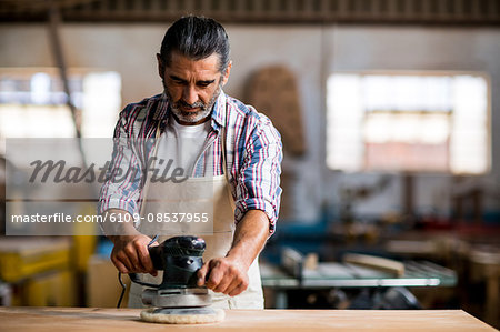 Carpenter polishing a wooden plank with polishing machine