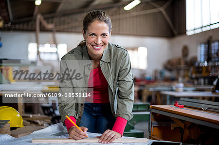 Female carpenter marking on wooden plank with pencil