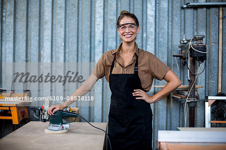 Portrait of female carpenter standing with polishing machine