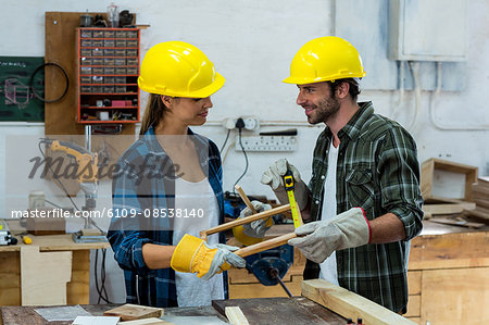 Male and female carpenters measuring a wooden plank