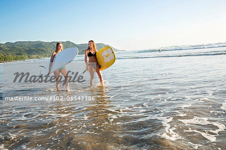 Two young women with surfboards wading in water