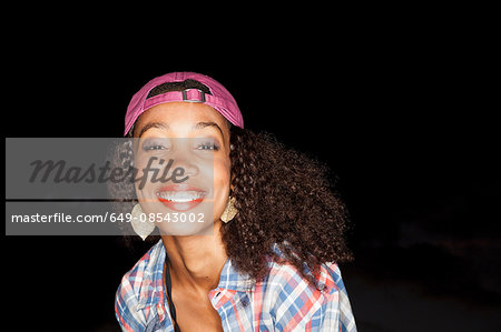 Portrait of young woman wearing baseball cap backwards looking at camera smiling