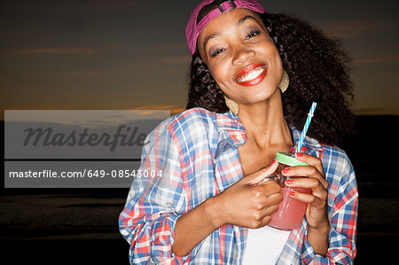 Young woman wearing baseball cap backwards holding mason jar looking at camera smiling