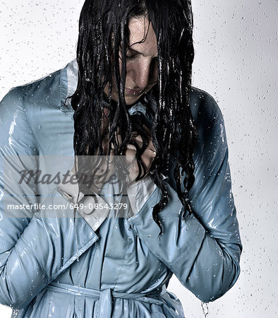 Woman wearing raincoat drenched in water looking down