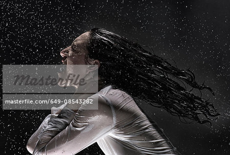 Side view of woman wearing white shirt drenched in rain throwing back hair