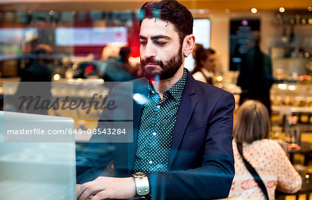 Businessman sitting in cafe window seat typing on laptop