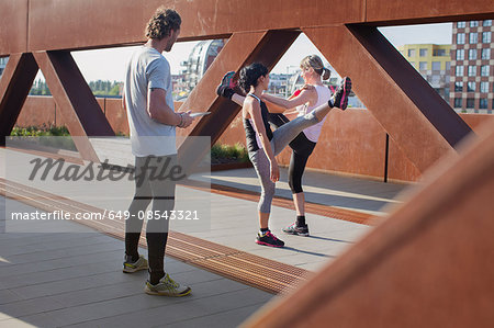 Two women training on urban footbridge with male personal trainer