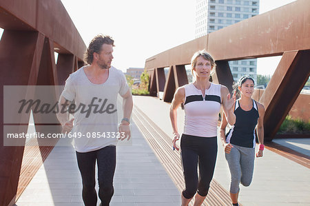 Female runners running on urban footbridge with personal trainer