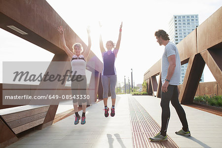 Two women jump training on urban footbridge with male personal trainer