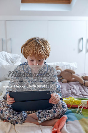 Boy in pyjamas using digital tablet in bed