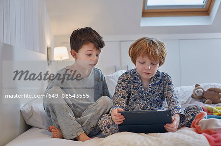 Boys in pyjamas using digital tablet in bed