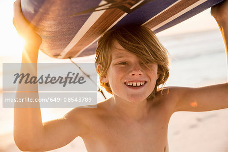 Boy carrying surfboard over head smiling