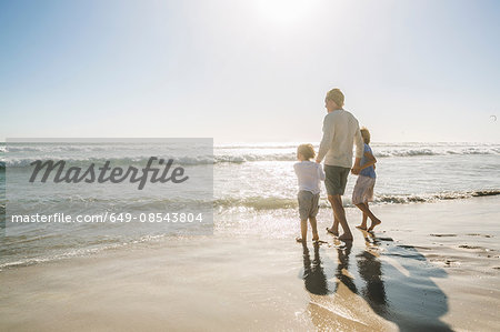 Rear view of father and sons on beach looking away at view