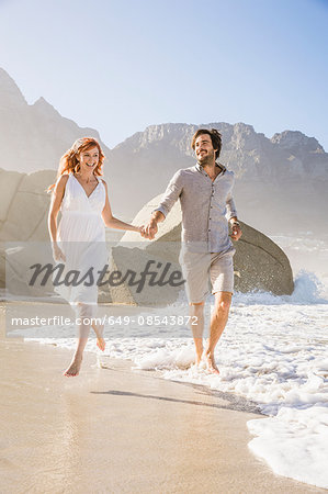 Full length front view of couple running on beach holding hands