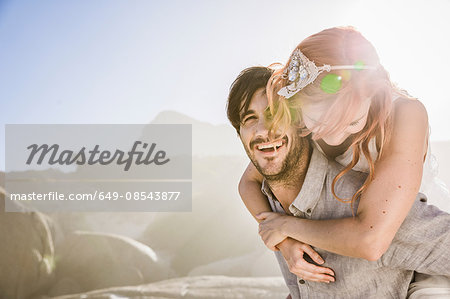 Man in front of rocks giving woman piggyback smiling