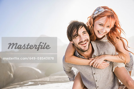 Man in front of rocks giving woman piggyback smiling