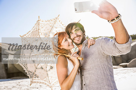 Couple on beach holding lace umbrella using smartphone to take selfie