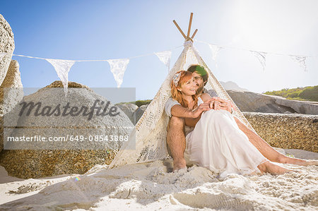 Couple on beach sitting in lace teepee smiling