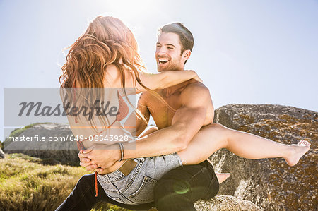 Couple outdoors, woman sitting on man's lap, face to face, laughing