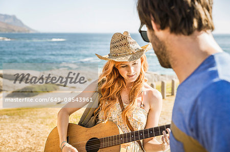 Mid adult couple on coast playing guitar, Cape Town, South Africa