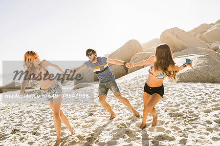 Three adult friends holding hands on beach, Cape Town, South Africa