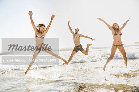 Three adult friends wearing bikini's and shorts jumping  in sea, Cape Town, South Africa