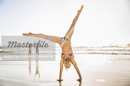 Mid adult woman wearing bikini cartwheeling on beach, Cape Town, South Africa