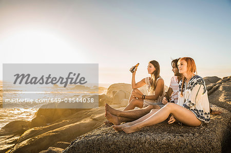 Three mid adults sitting on beach looking out at sunset, Cape Town, South Africa