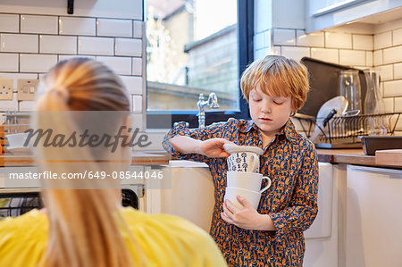 Boy carrying stack of mugs in kitchen