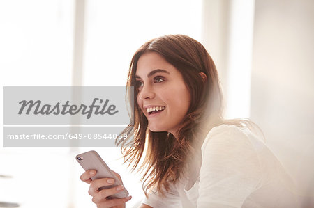 Happy young woman using smartphone in front of window